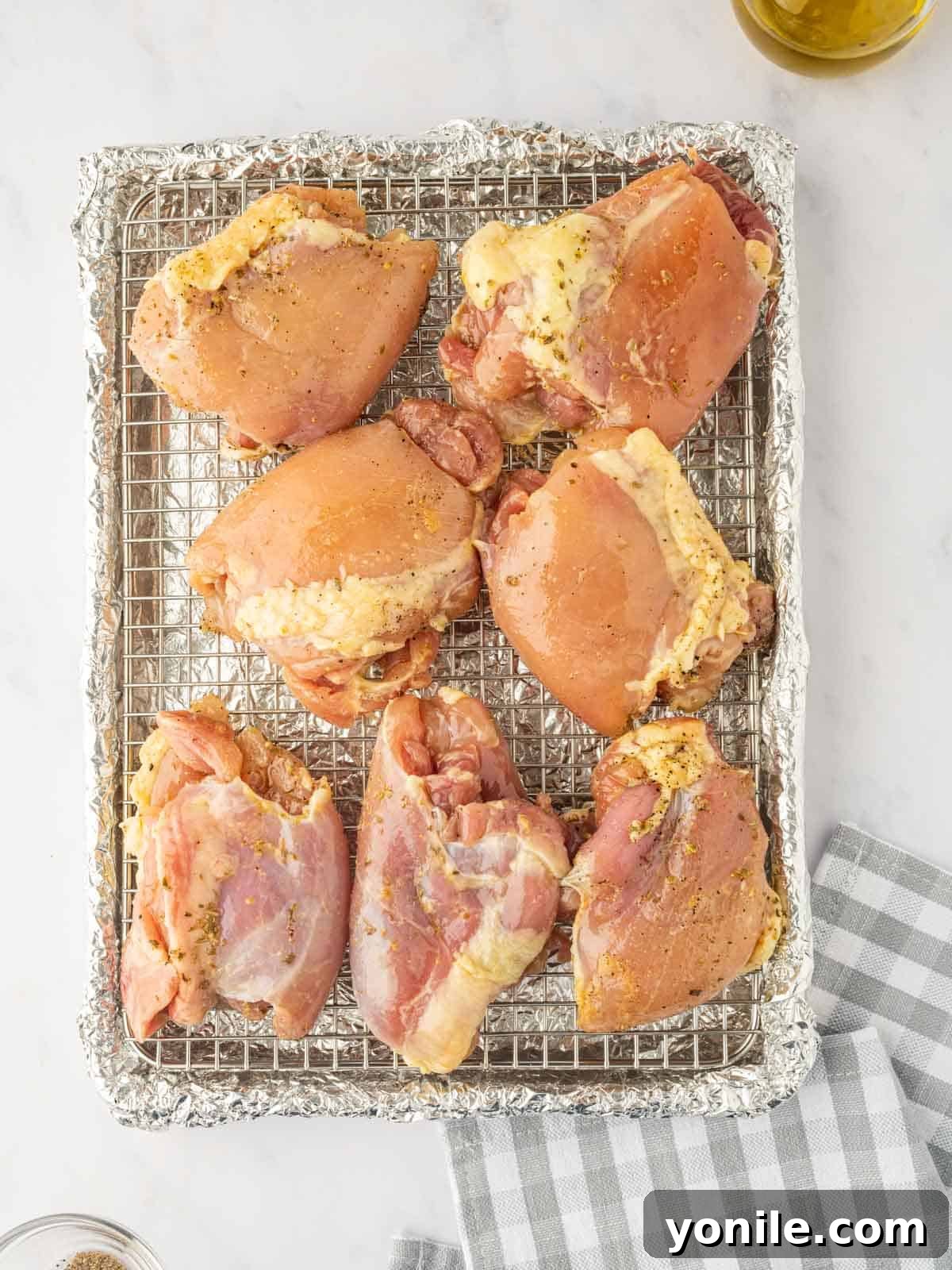 Seasoned chicken thighs are neatly arranged on a wire rack set over a foil-lined baking tray, ready for baking.