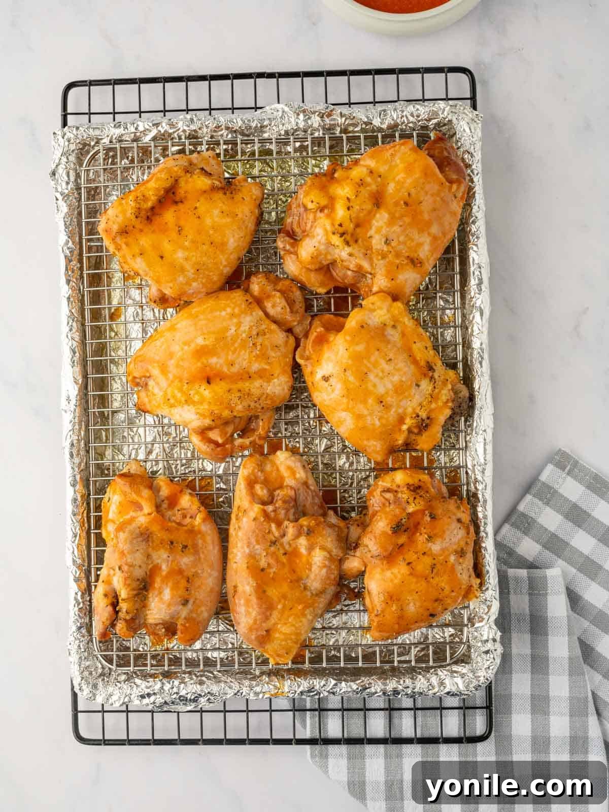 Baked chicken thighs are being brushed generously with a rich, glossy buffalo sauce.