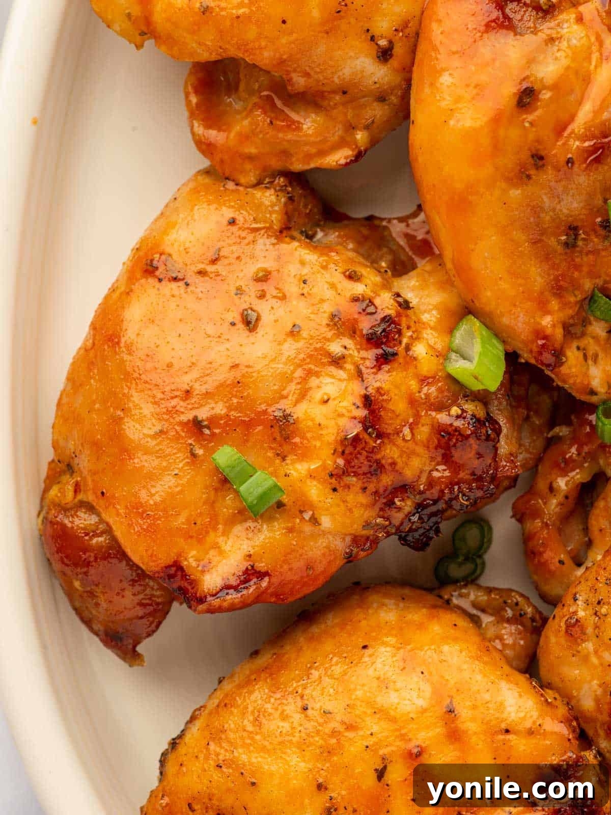 A close-up view of a plate of baked buffalo chicken thighs, generously coated in sauce, garnished with fresh green onions.