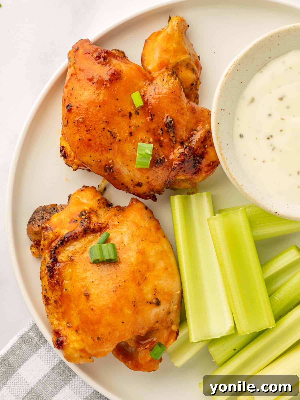 A plate featuring two spicy buffalo chicken thighs, accompanied by crisp celery sticks and a side of creamy dressing.