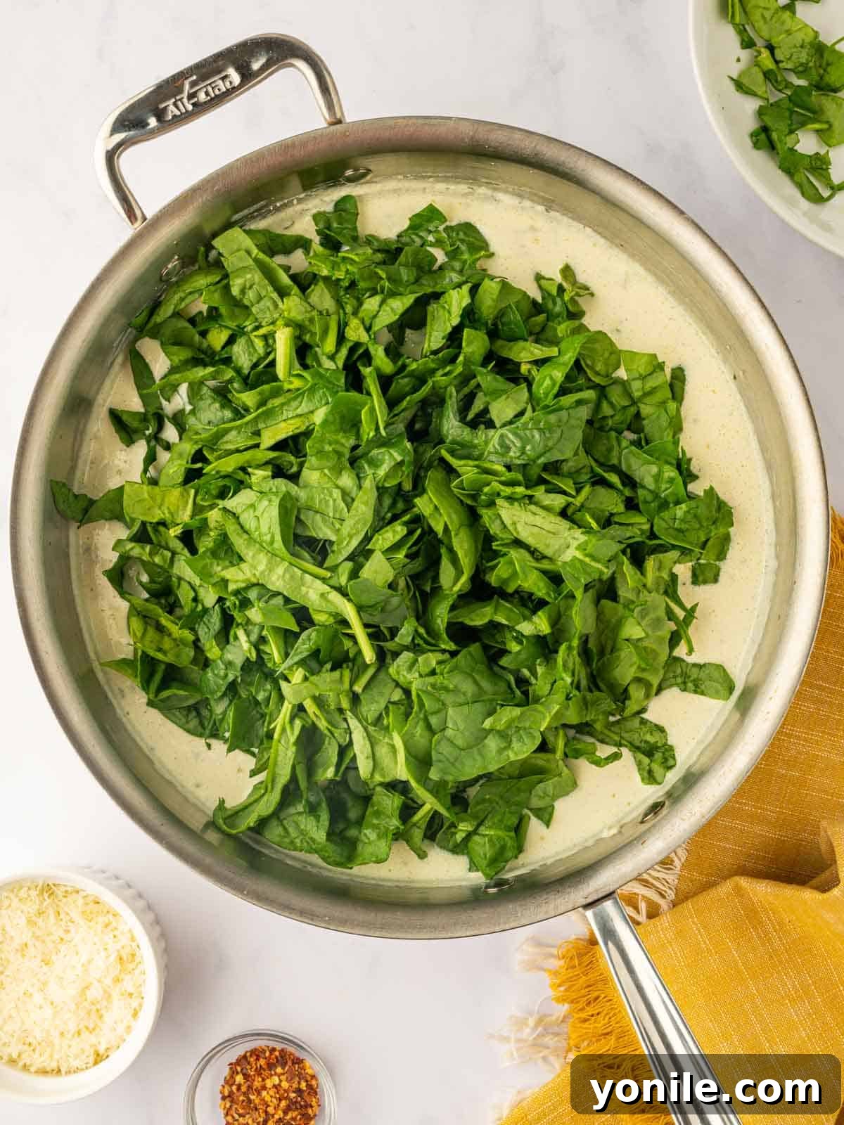 Spinach wilts in a skillet of cream sauce.