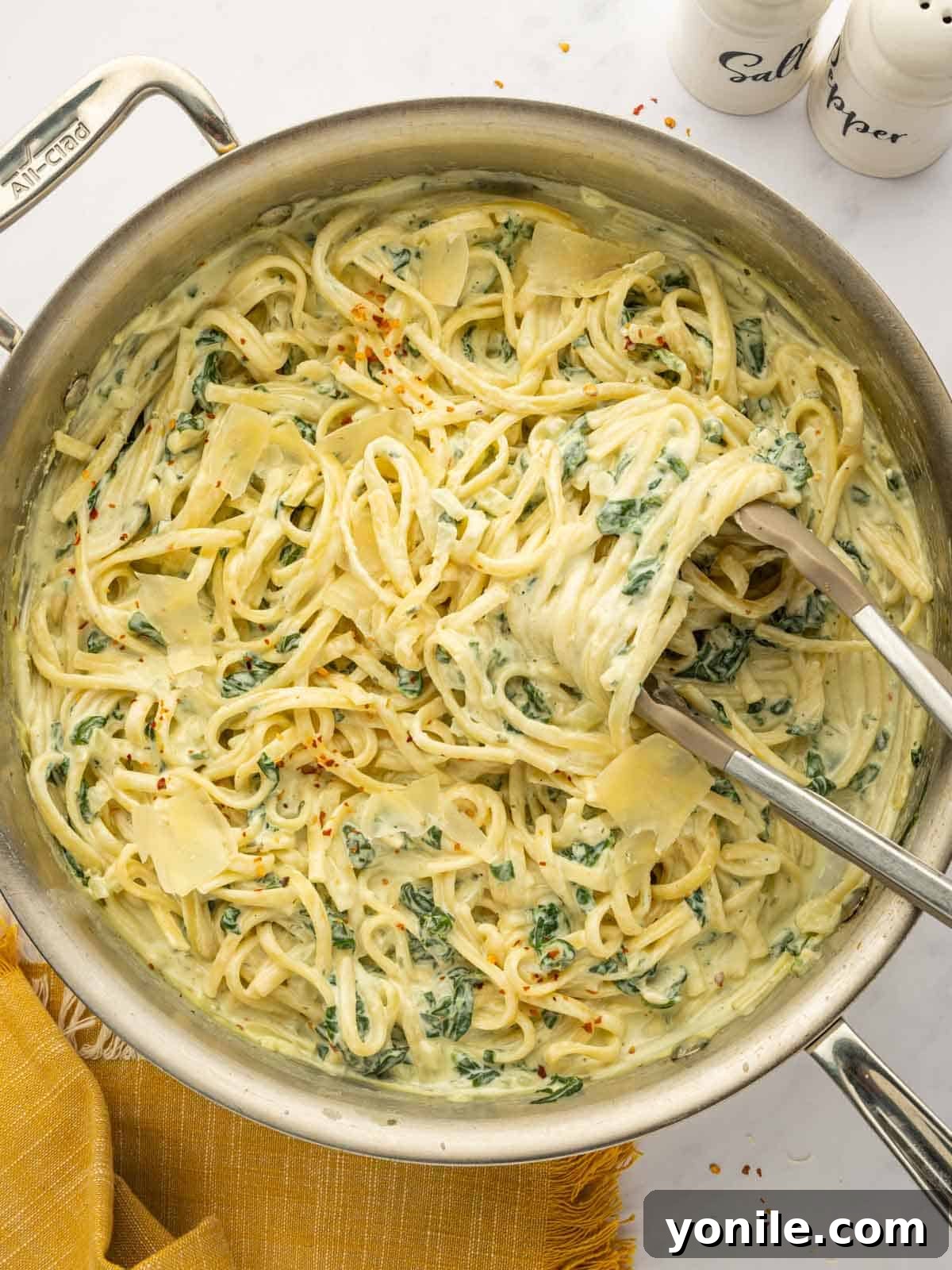 Tongs toss boursin cheese pasta in a skillet.