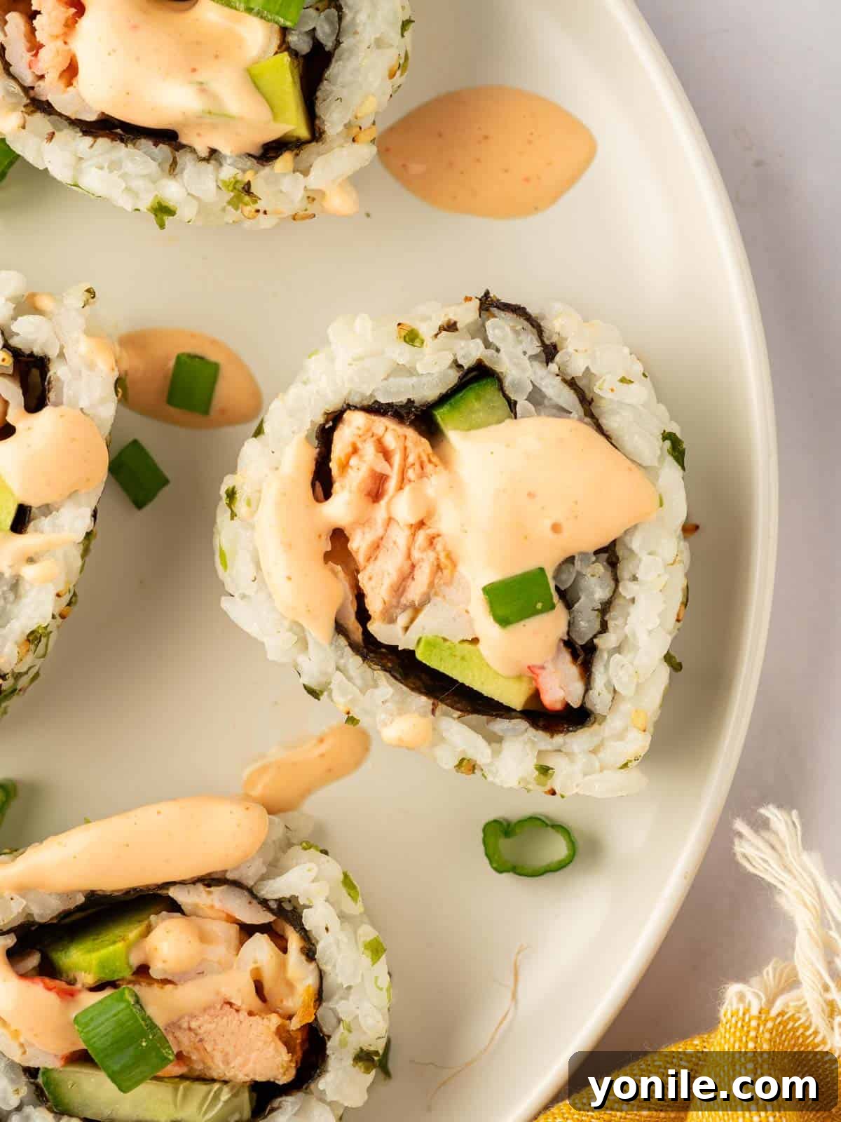 Dynamite Salmon Roll 15 A single piece of perfectly crafted salmon sushi is topped with a swirl of spicy mayo, ready to be eaten.