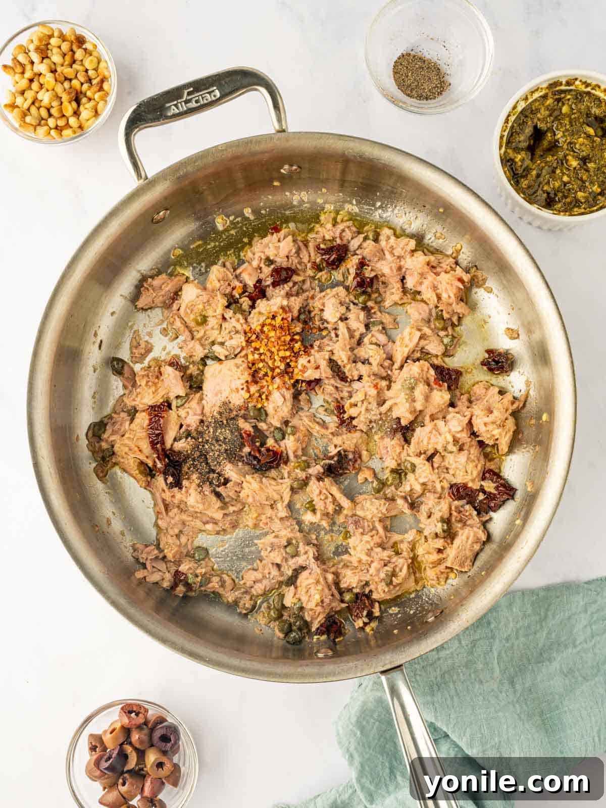 Flaky canned tuna is gently stirred into a sizzling skillet with sun-dried tomatoes and capers, absorbing the rich aromatic flavors.