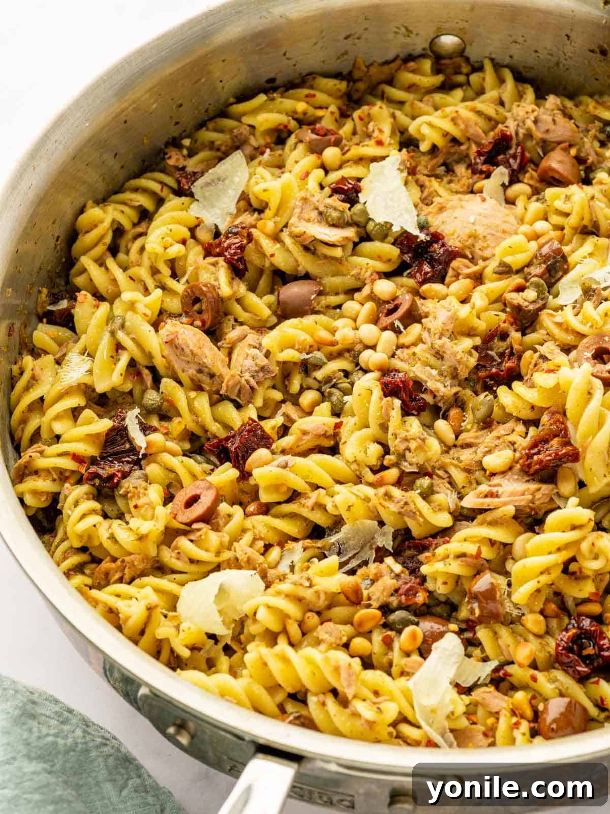 A generous serving of Tuna Pesto Pasta, topped with an abundance of shaved Parmesan cheese, sits in a skillet ready to be devoured.