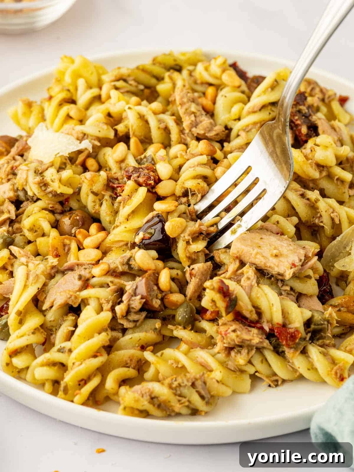 A fork lifts a savory bite of tuna pasta, showcasing the rich pesto sauce, flaky tuna, and al dente noodles.
