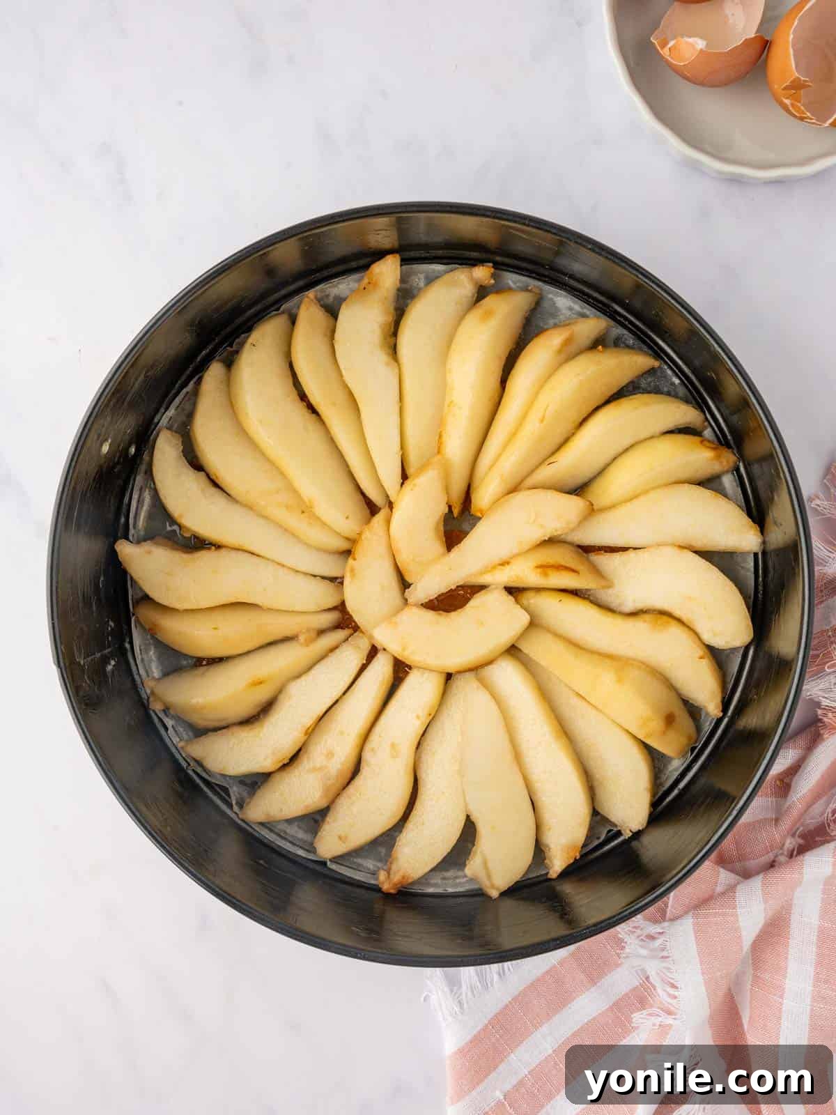 Pear slices are artfully arranged in a circular pattern over the caramel in a cake pan.