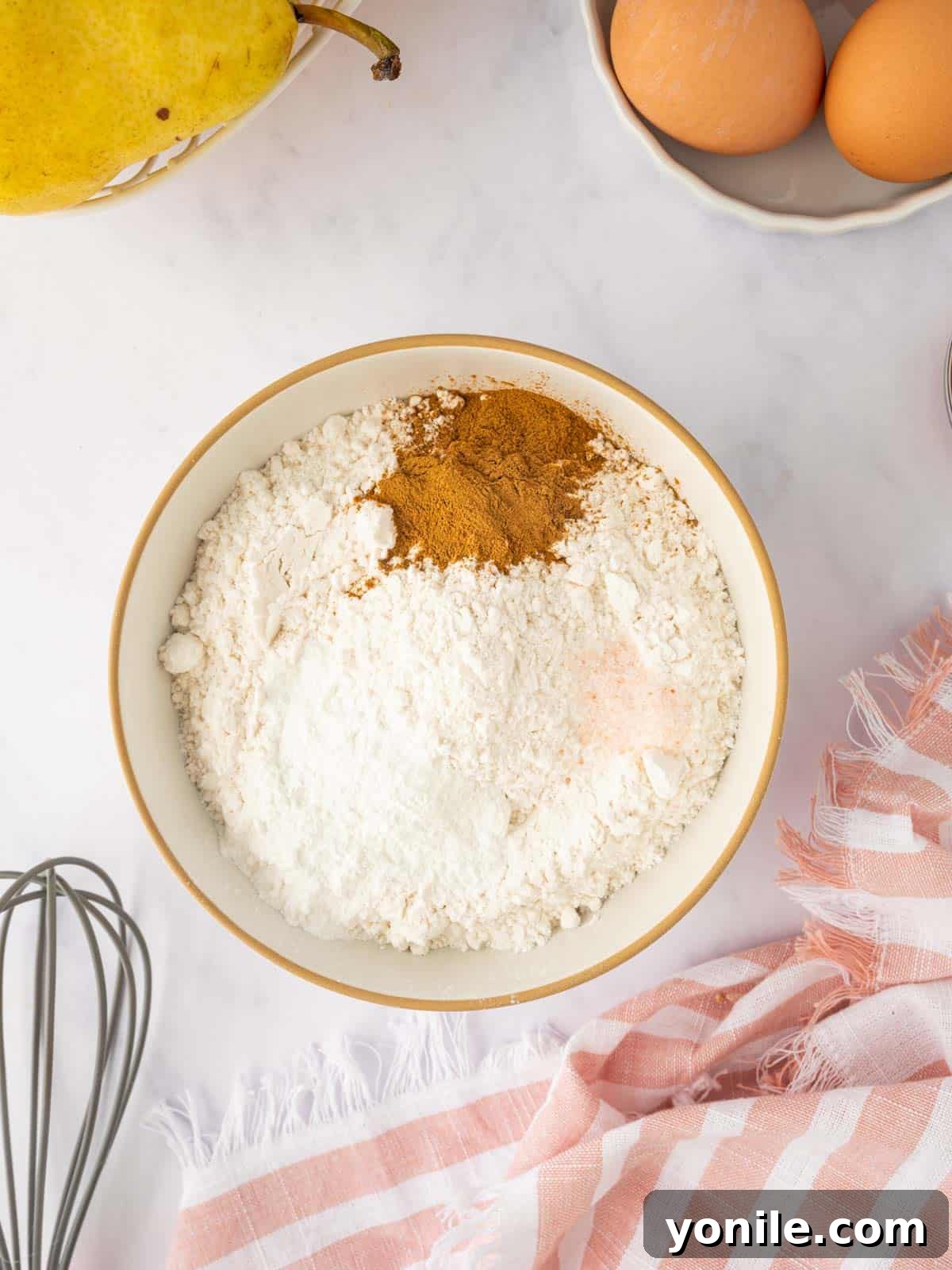 Dry cake ingredients, including flour and spices, are whisked together in a bowl.