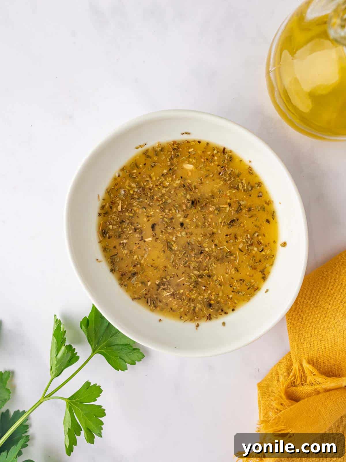 A bowl of vinaigrette for bean salad. A small clear bowl filled with a golden Greek vinaigrette dressing, showing the mix of olive oil, herbs, and spices.