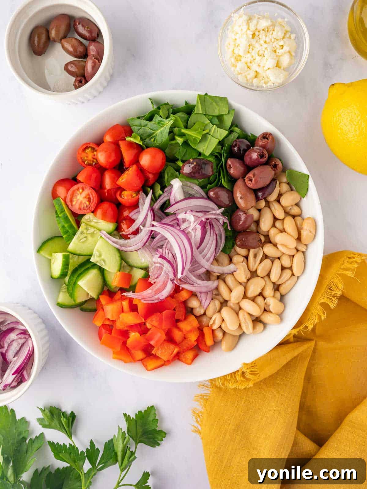 Ingredients for Greek bean salad are in a bowl. A large mixing bowl filled with the fresh, colorful salad ingredients before dressing, including spinach, beans, peppers, and tomatoes.