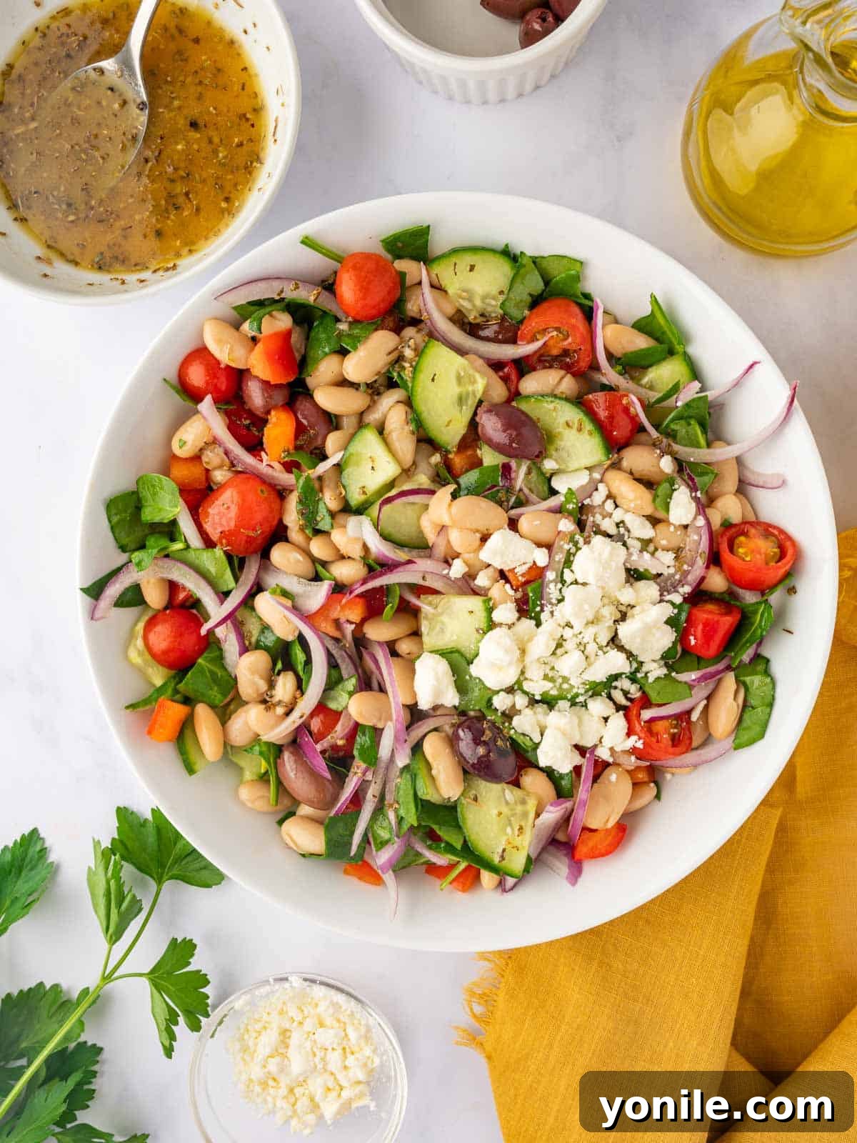 Added feta cheese to the bean salad bowl. The Greek bean salad, now mixed with dressing, has crumbled feta cheese sprinkled over the top, ready for a final toss.