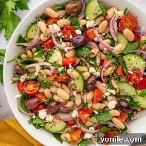 A large bowl of salad with beans and veggies. A close-up view of the prepared Greek White Bean Salad, showcasing the colorful mix of ingredients in a rustic bowl.