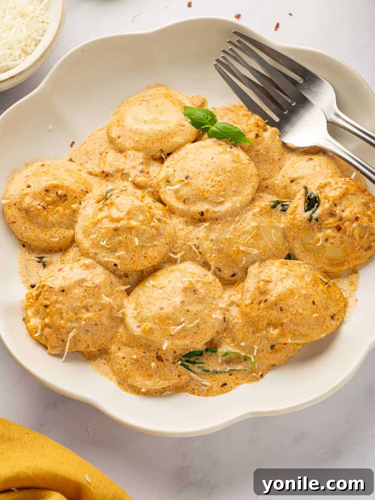 A fork rests beside a plate of ravioli topped with a creamy red sauce, garnished with fresh basil.
