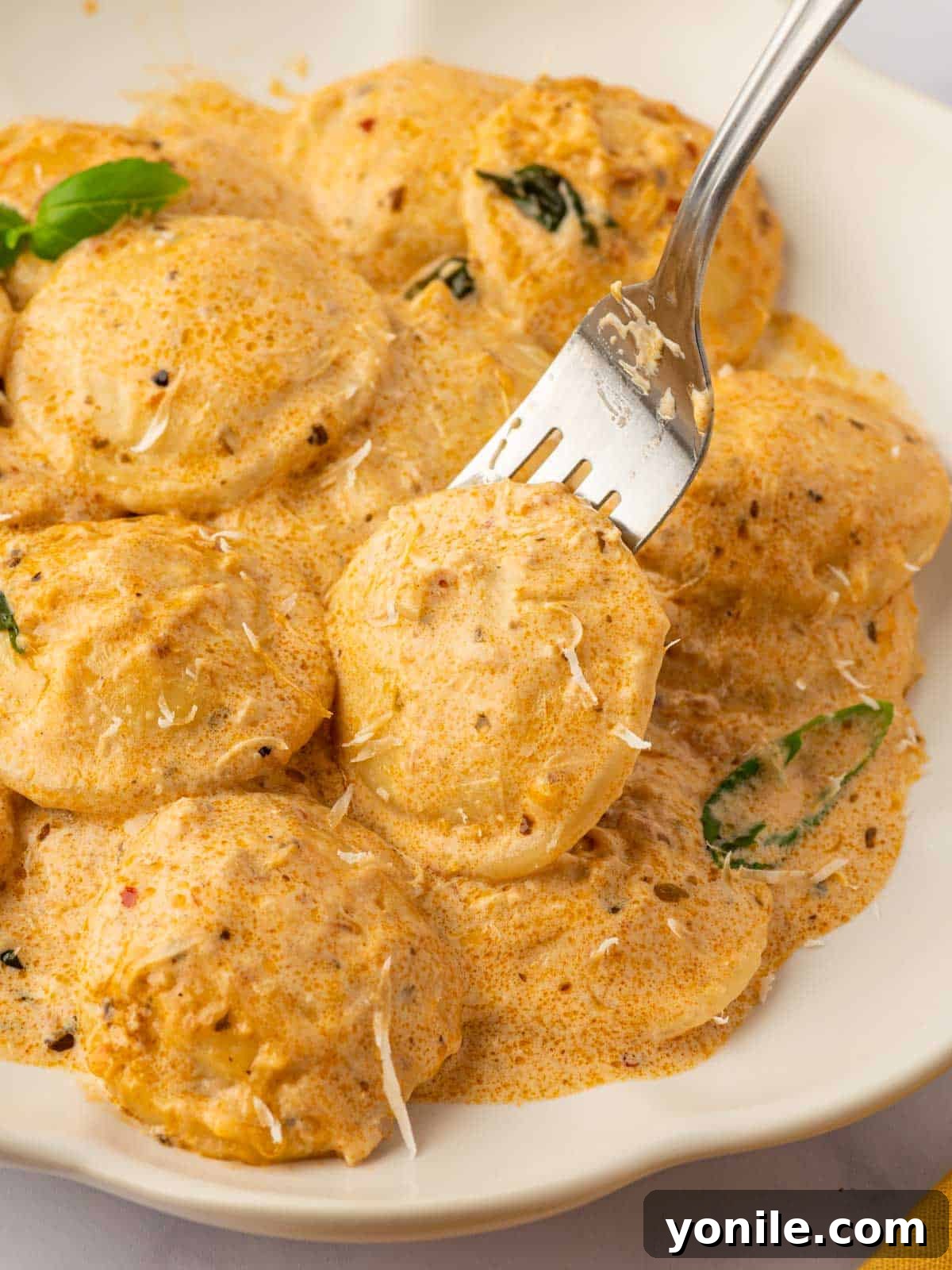 A fork lifting a piece of sun-dried tomato ravioli from a plate, showing the creamy sauce.