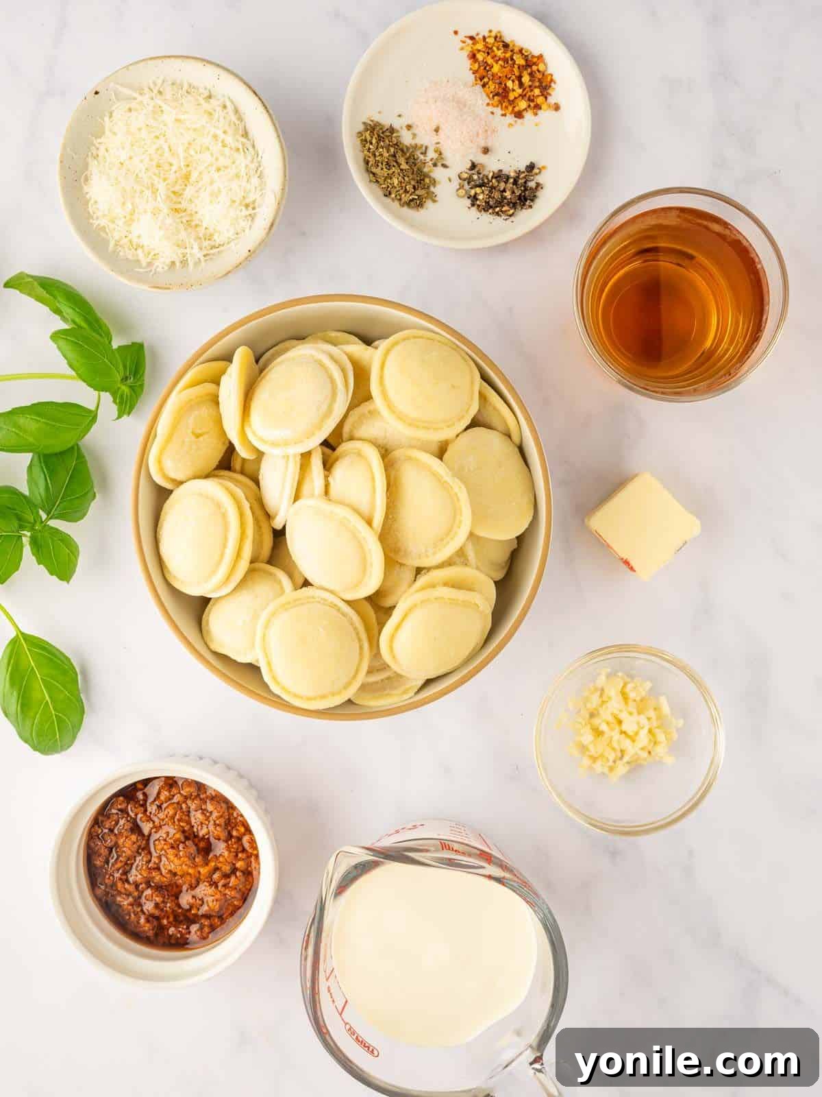 Various ingredients for cheese ravioli pasta laid out on a white surface.