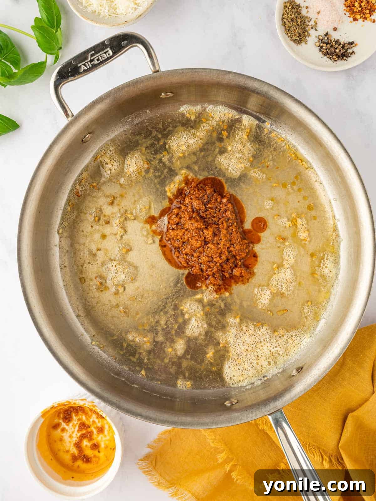 Sun-dried tomato pesto being stirred into sautéed garlic in a pan.