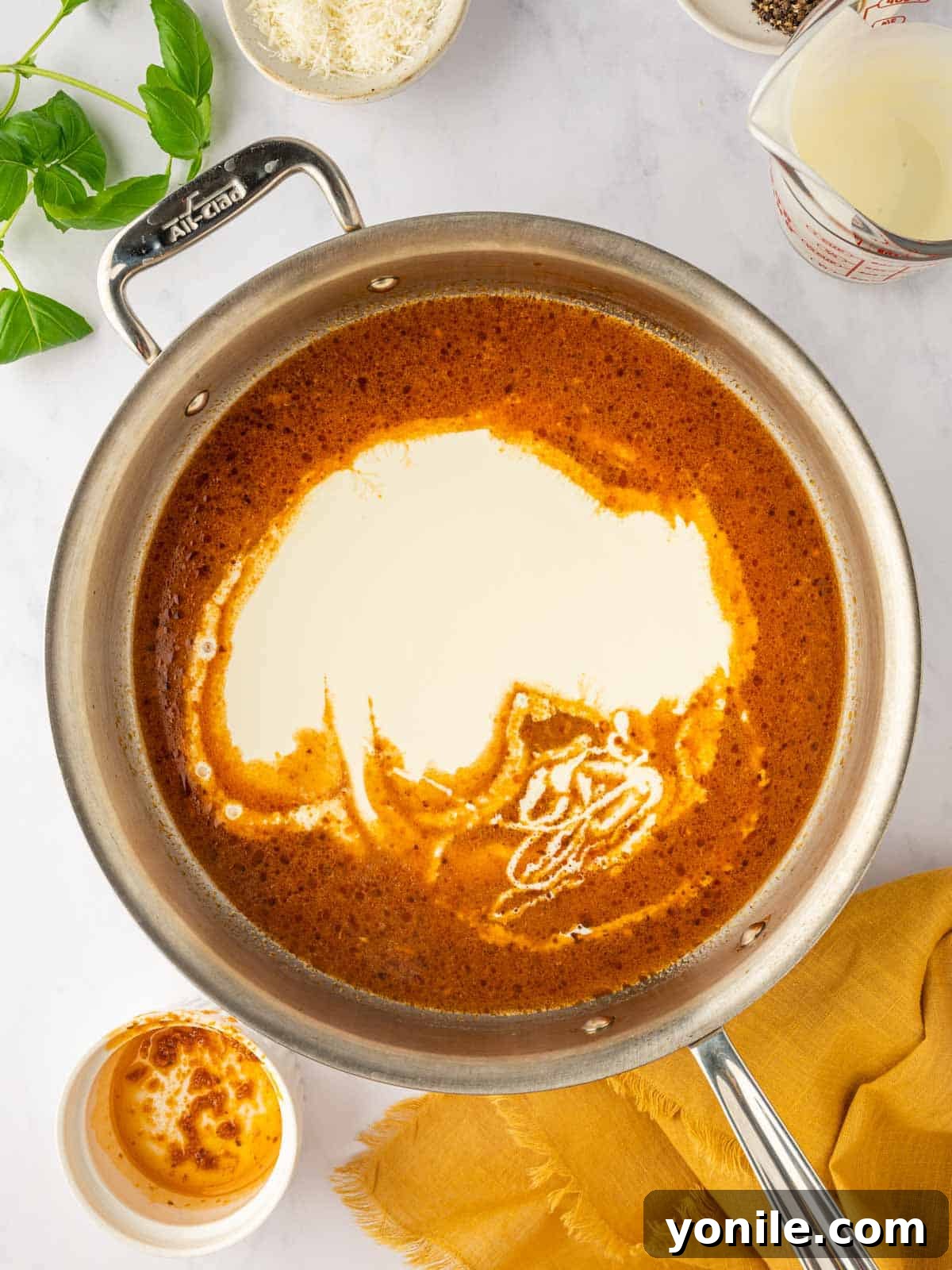 Heavy cream being poured into a red tomato sauce in a skillet.
