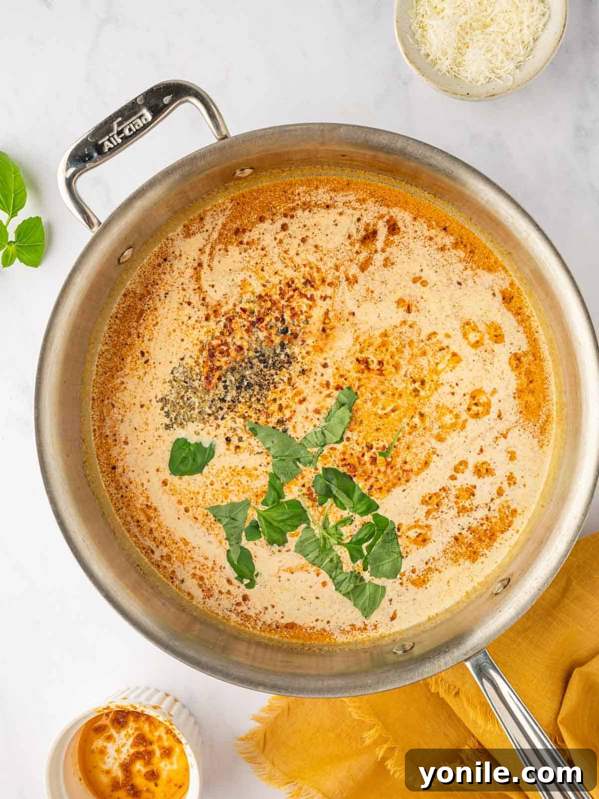 Fresh basil leaves being sprinkled over the simmering tomato cream sauce.