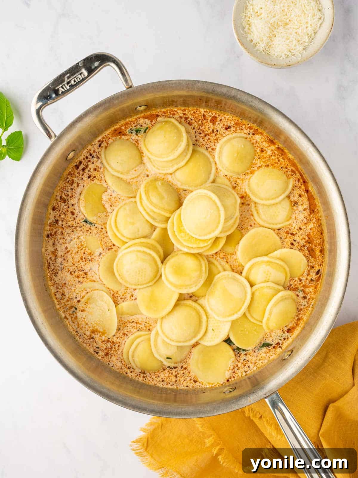 Cooked four cheese ravioli being added directly into the sun-dried tomato cream sauce in a large skillet.