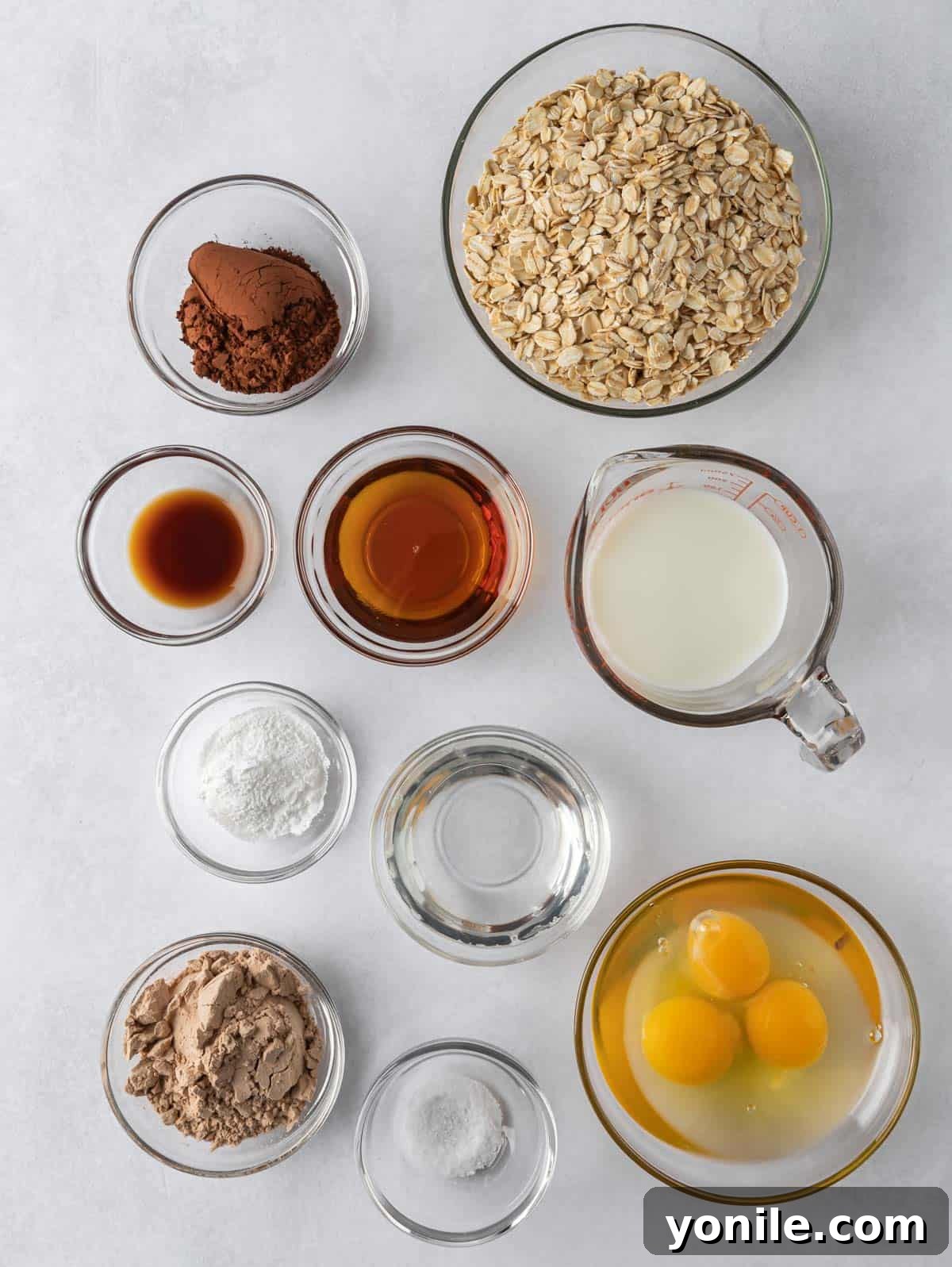 All the fresh ingredients laid out on a clean counter, ready for making chocolate protein pancakes, including oats, protein powder, eggs, milk, and cocoa powder.