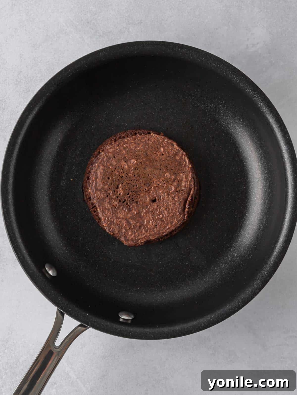 A perfectly formed chocolate protein pancake sizzling and browning on a hot nonstick skillet.