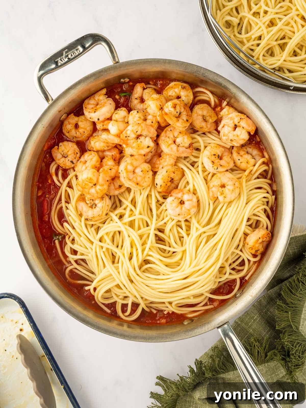 Prawn Pasta Perfection 9 Cooked spaghetti, shrimp, and rich tomato sauce being combined in a large skillet.