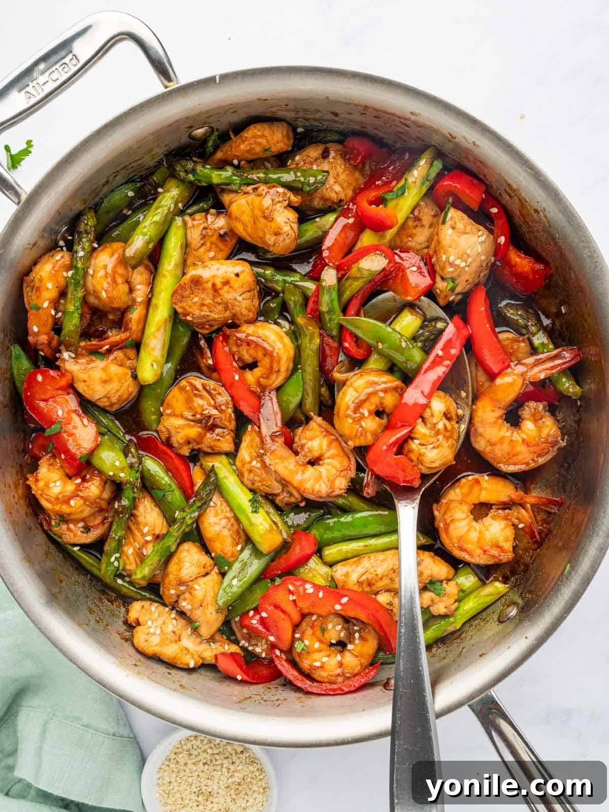 Sizzling Surf and Turf Stir-Fry 9 A close-up shot of a spoon lifting a portion of Chicken and Shrimp Stir Fry from a large skillet, showing the glossy sauce clinging to the chicken, shrimp, and vegetables.