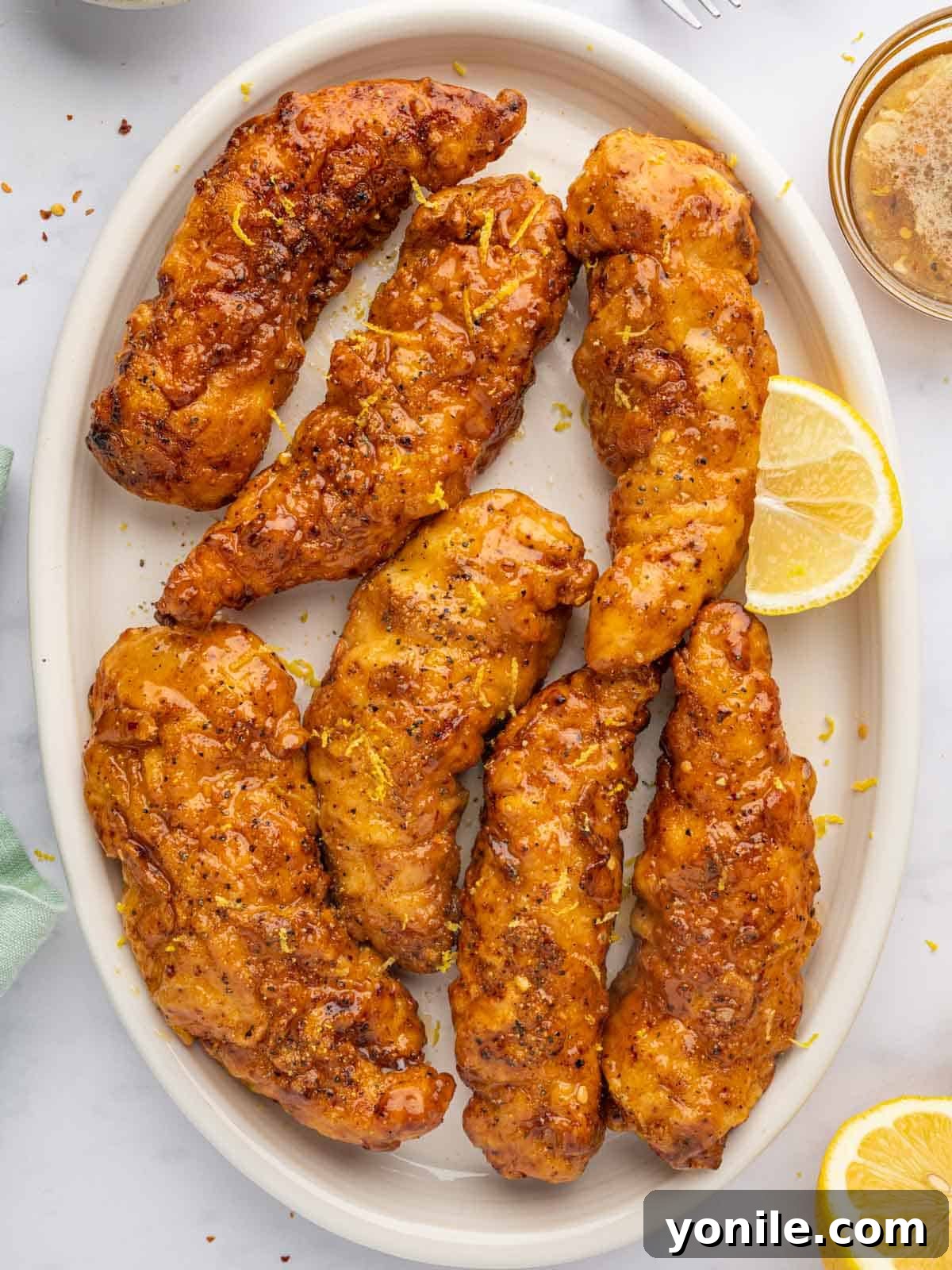 Zesty Lemon Pepper Chicken Tenders 2 Crispy fried lemon pepper chicken strips with a sticky honey glaze, garnished with fresh lemon slices and parsley.