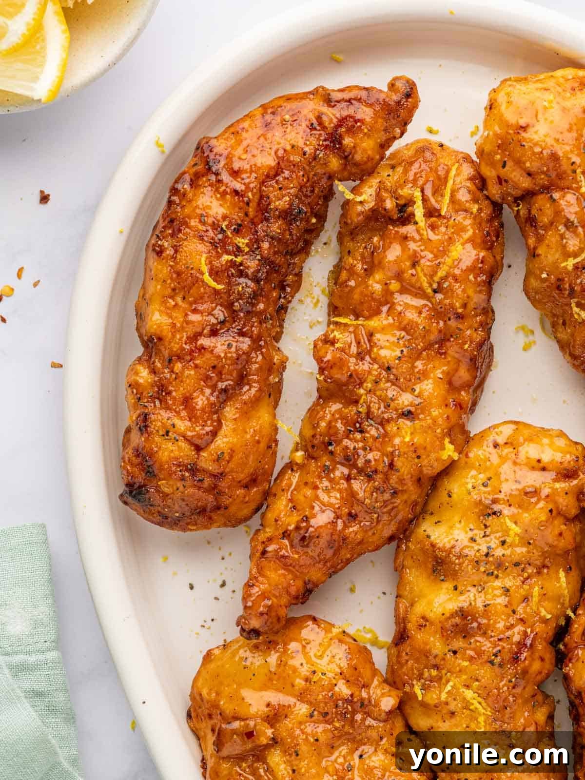 Zesty Lemon Pepper Chicken Tenders 12 A vibrant platter of glazed lemon pepper chicken strips, garnished with fresh lemon wedges.