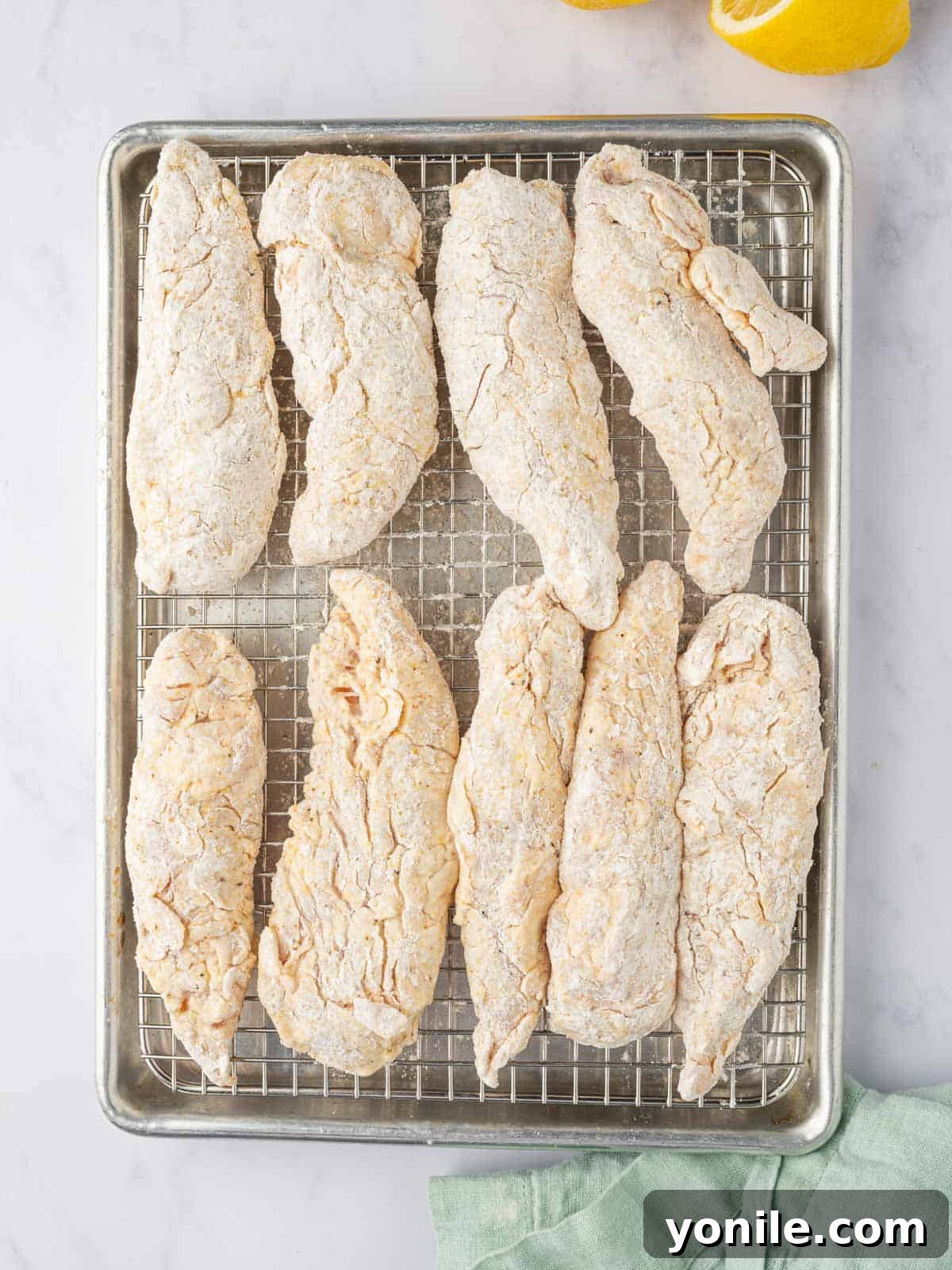 Zesty Lemon Pepper Chicken Tenders 6 Breaded raw chicken tenders resting on a wire rack, ready for frying.