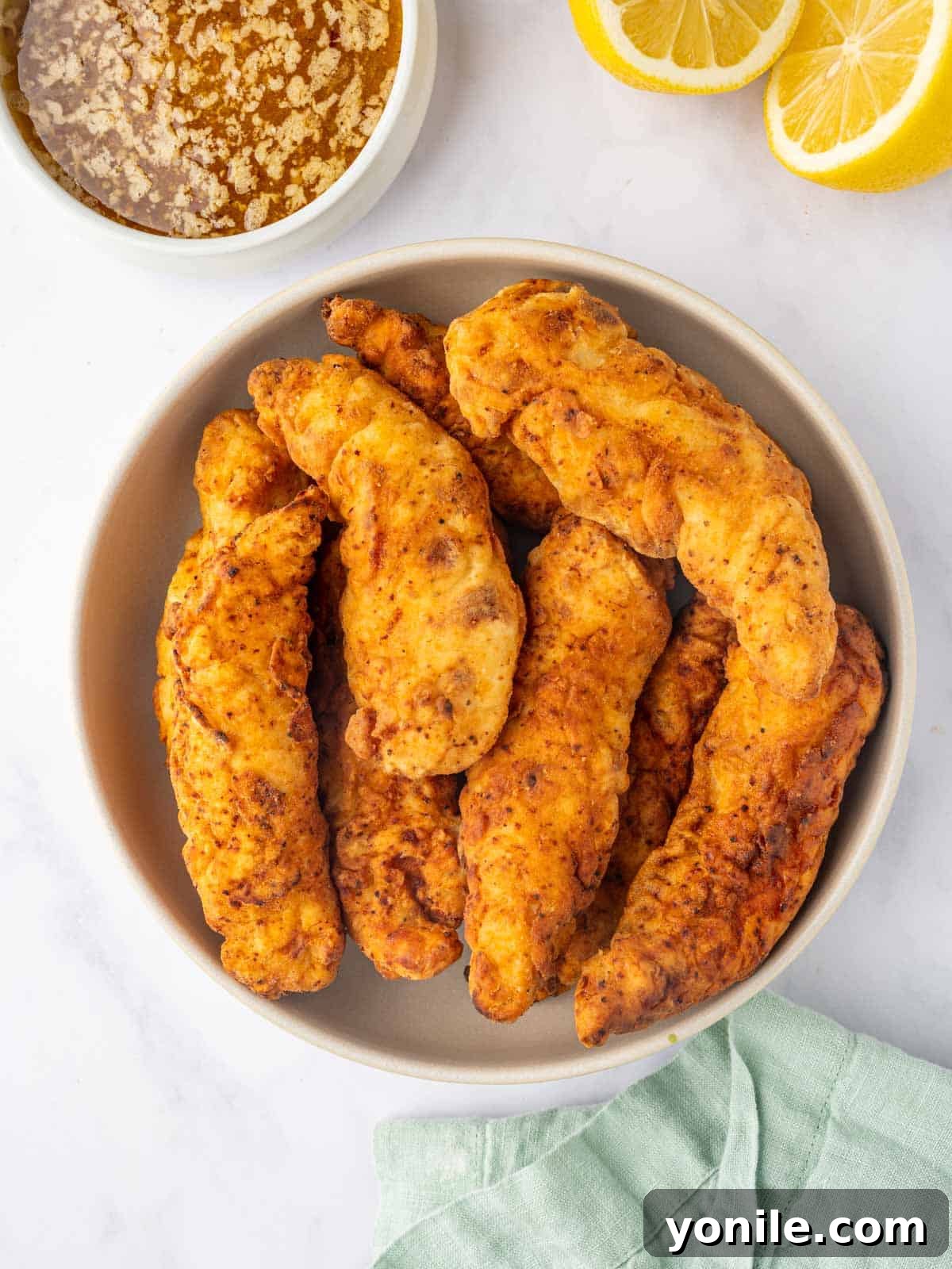 Zesty Lemon Pepper Chicken Tenders 7 A bowl filled with golden-brown fried chicken strips, ready for glazing.