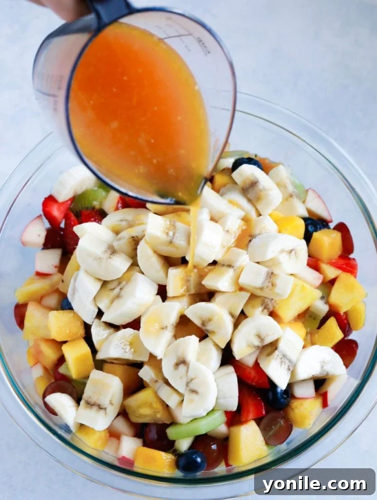 Effortless Fruit Fiesta 3 A stream of fragrant orange blossom honey dressing being poured gracefully over a bowl of freshly chopped fruits.