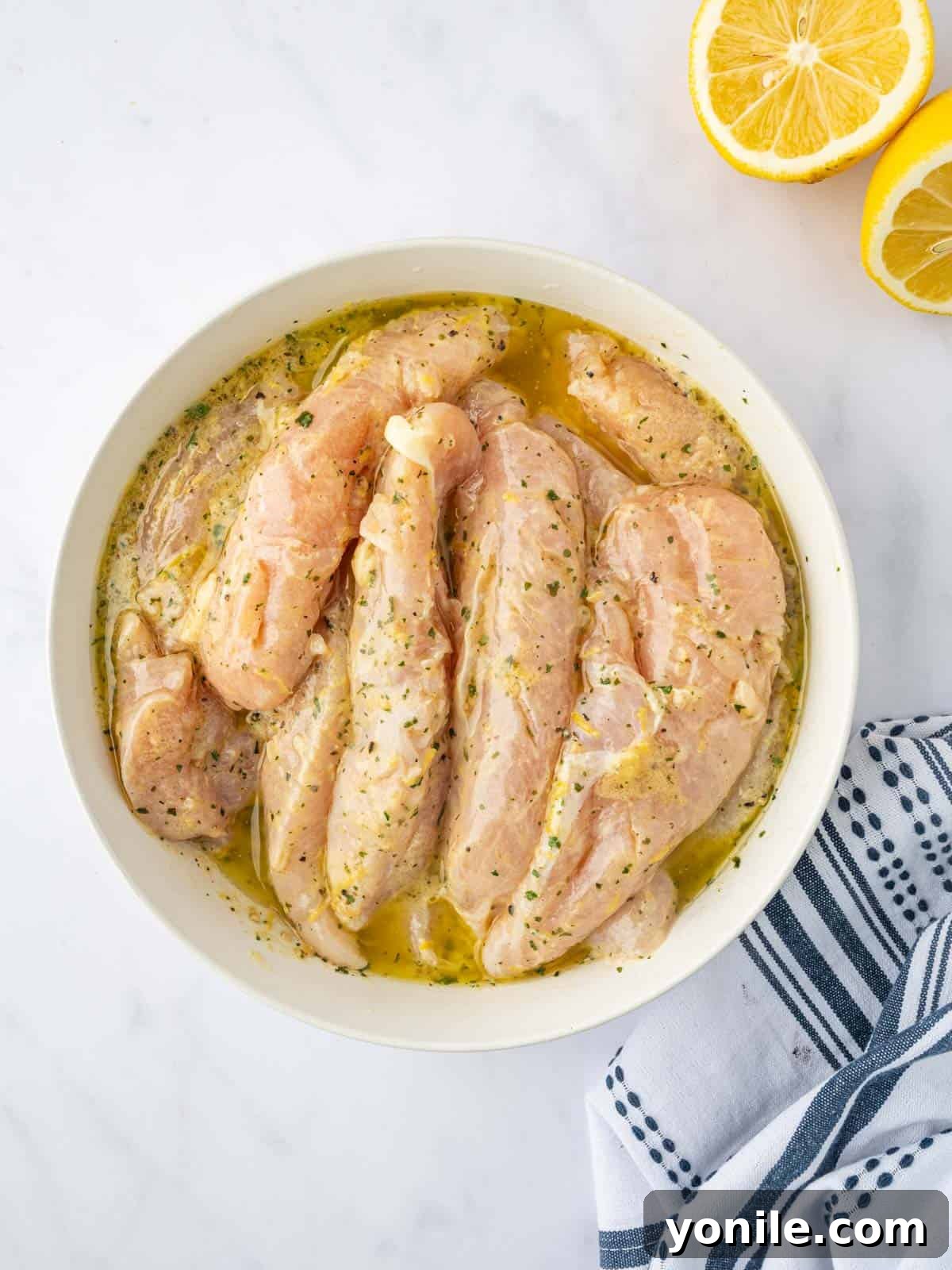 Chicken marinates in a lemon pepper seasoning blend in a bowl.