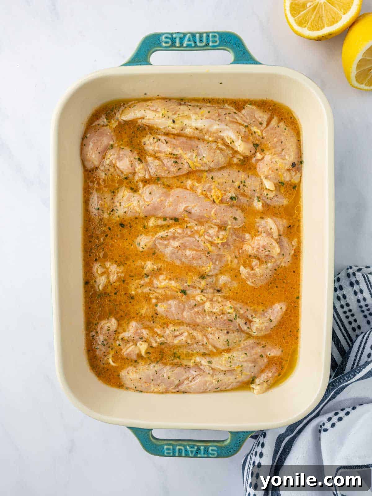 Chicken is prepared for baking in a baking dish with lemon pepper sauce.