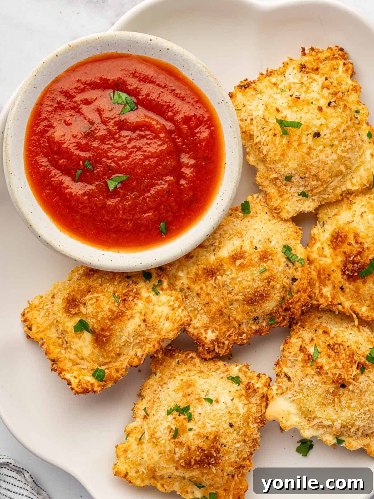 Crispy Air Fryer Ravioli 11 Air fried ravioli on a plate with a small bowl of marinara.