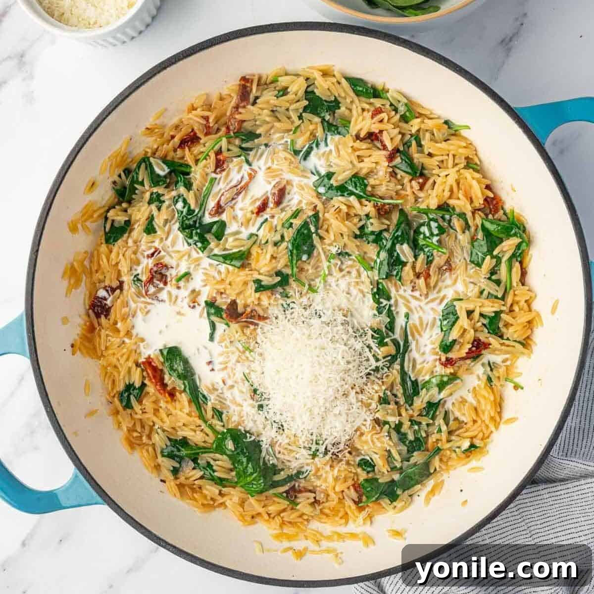 Grated Parmesan cheese being stirred into a bowl of creamy orzo pasta.