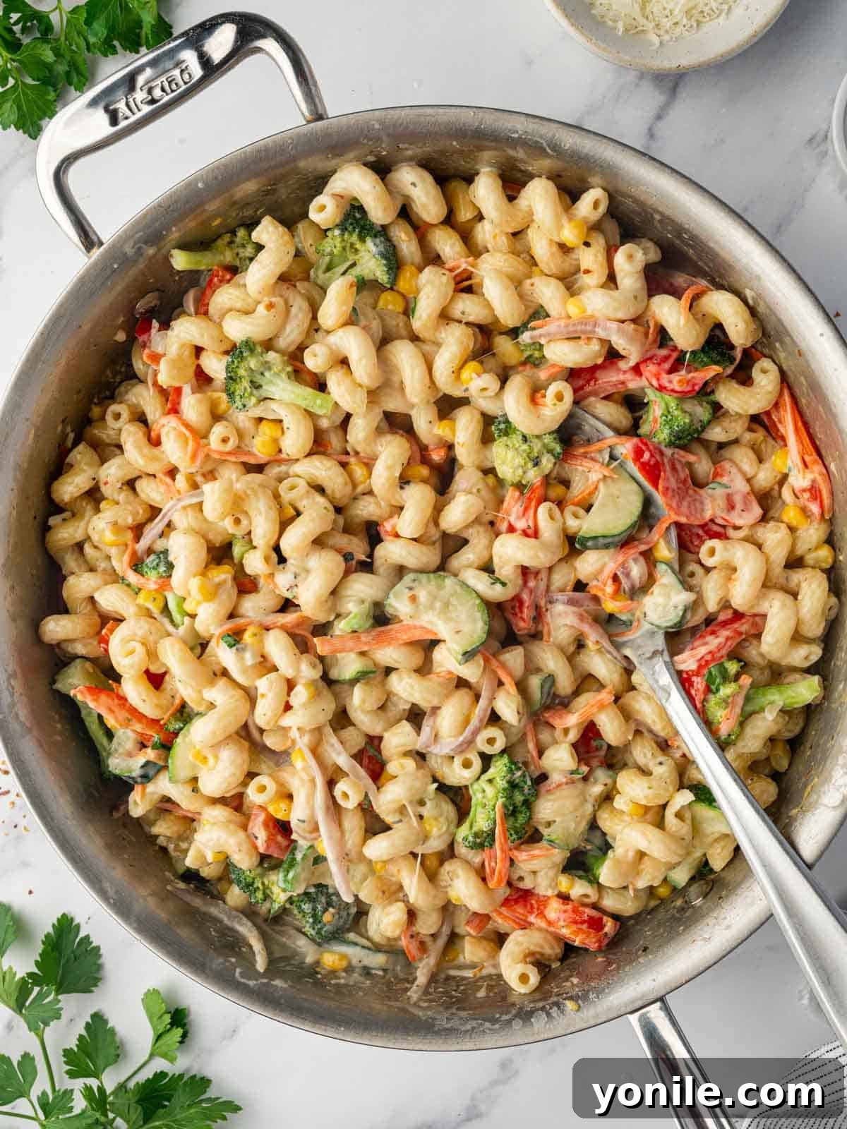 A spoon serves cheesy pasta with vegetable from a skillet, showcasing a generous portion of creamy veggie pasta.