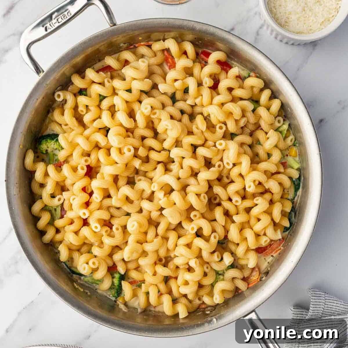 Cooked pasta is added to the sautéed veggies and creamy sauce in the skillet.