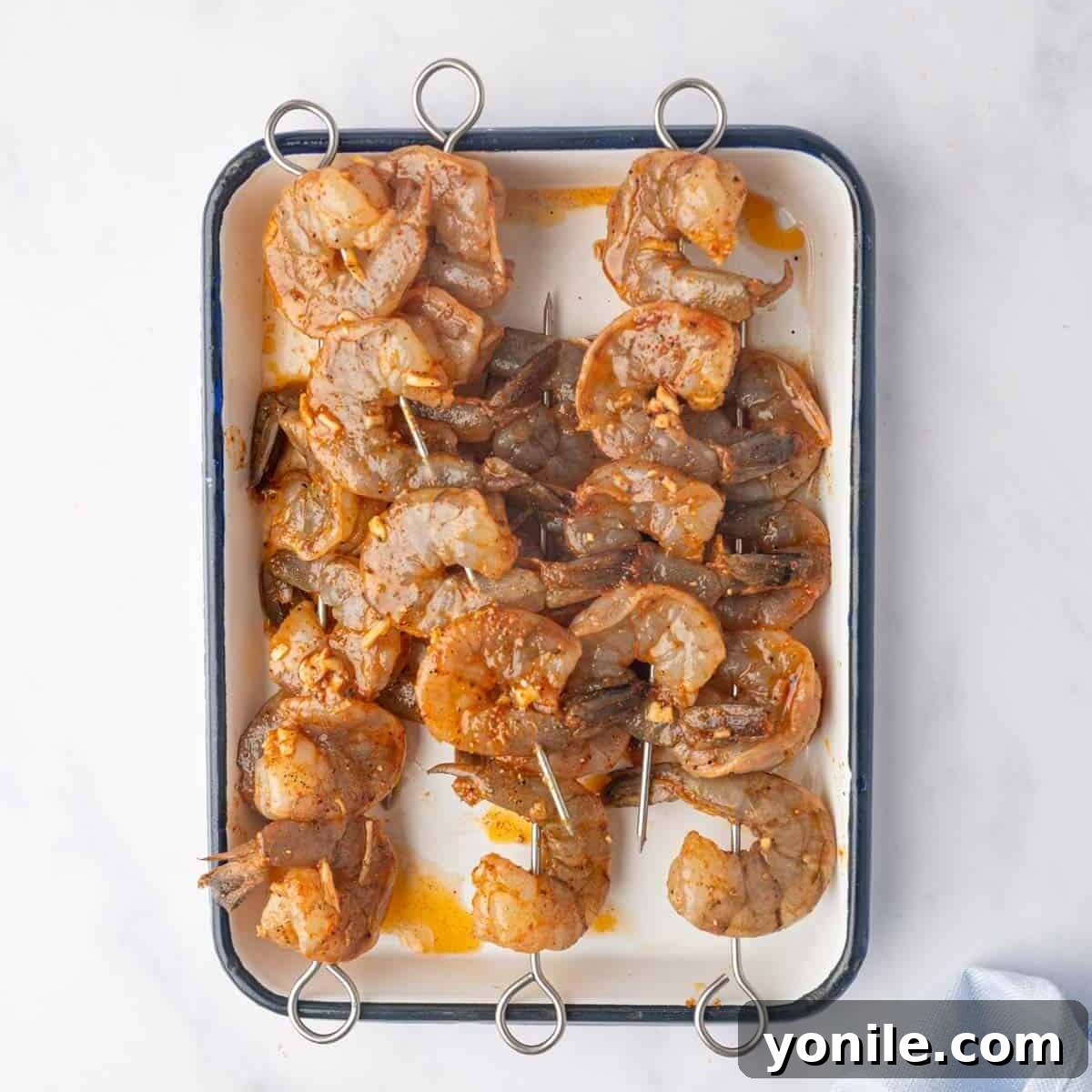 Marinated shrimp being threaded onto skewers before grilling.