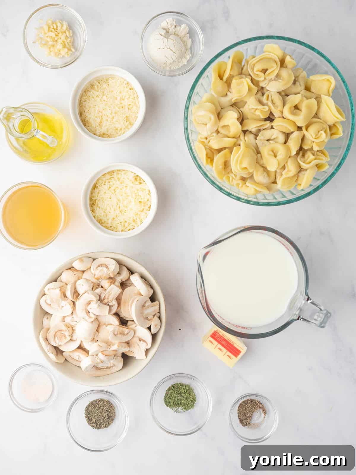Creamy Cheese Tortellini Alfredo 3 A selection of fresh ingredients laid out on a table, including cheese tortellini, cremini mushrooms, butter, garlic, milk, and various seasonings.