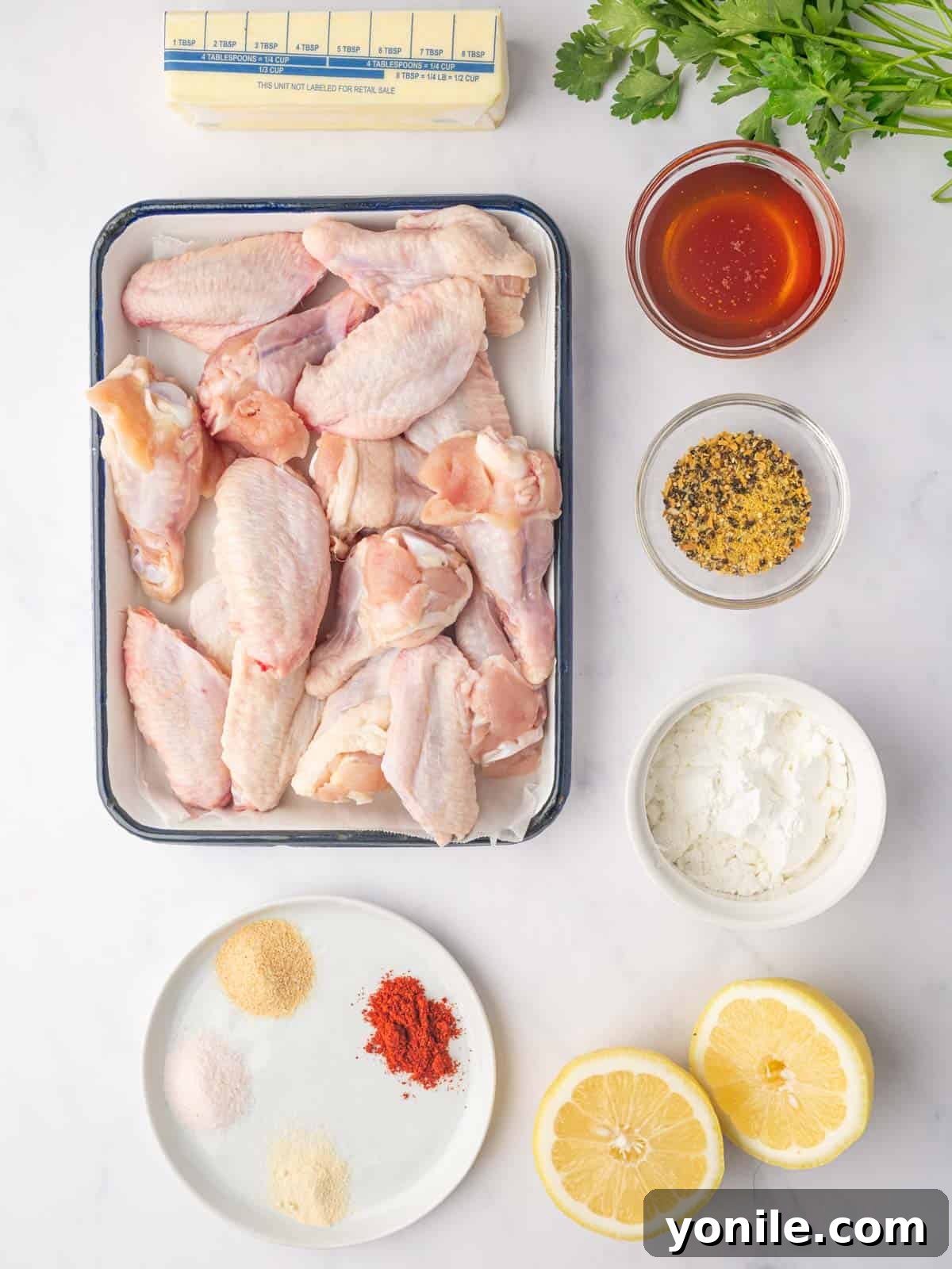 A flat lay of fresh ingredients laid out for making Honey Lemon Pepper Wings, including chicken wings, lemon, honey, butter, and various spices.