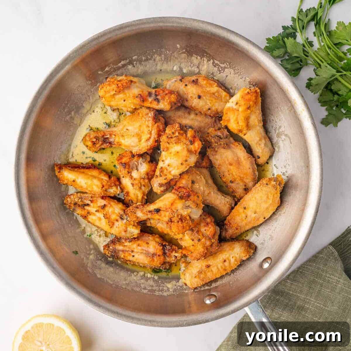 Freshly baked chicken wings being tossed with the sticky honey lemon pepper sauce in a large bowl.