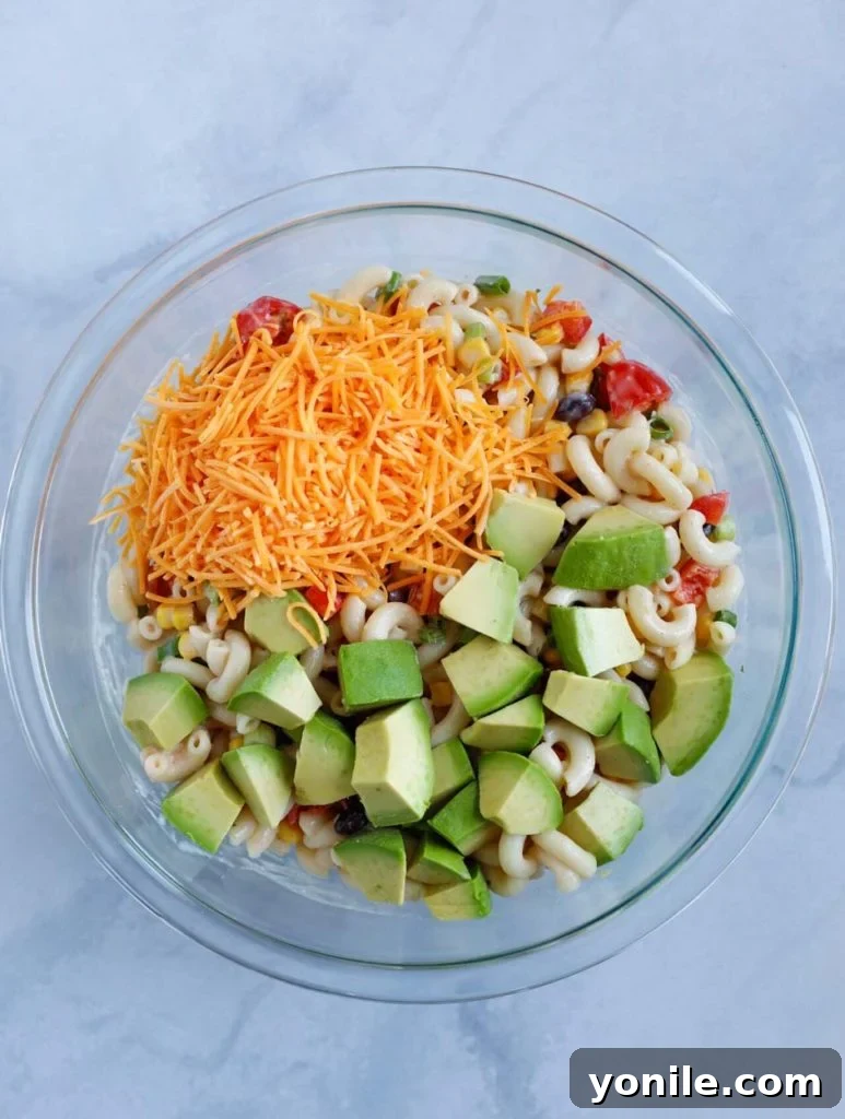 All the freshly prepared ingredients for Taco Ranch Pasta Salad, including cooked elbow pasta, chopped vegetables, and seasoning, gathered in a large glass mixing bowl, ready to be dressed.