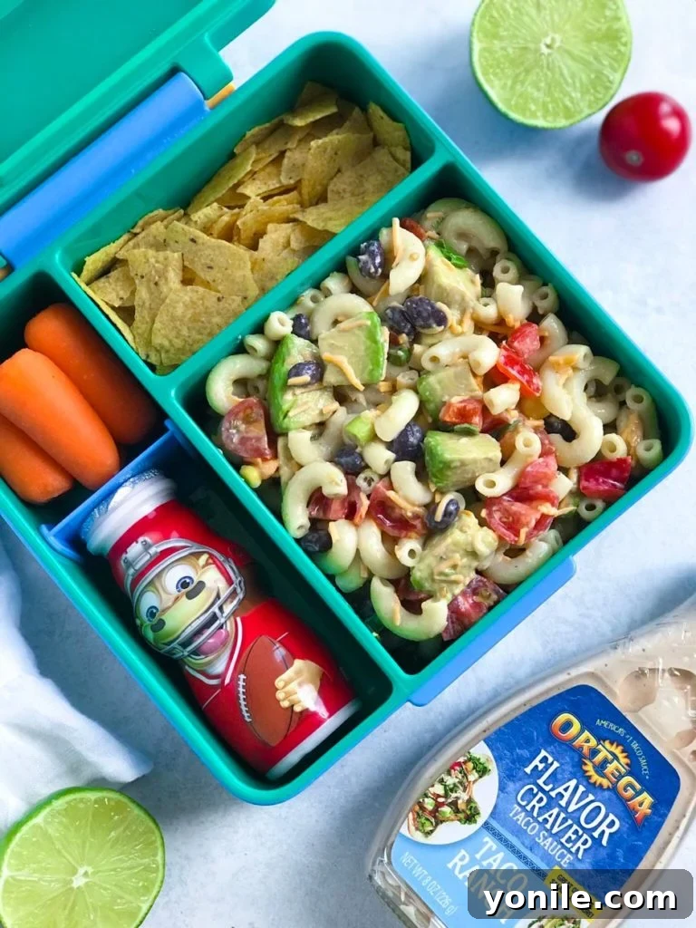 A delightful portion of Taco Ranch Pasta Salad neatly packed in a lunchbox, accompanied by a side of broken taco shells and a small container of extra dressing, perfect for a balanced meal on the go.