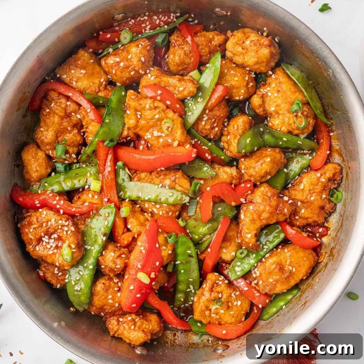 A skillet with sesame seed garnished chicken and vegetables.