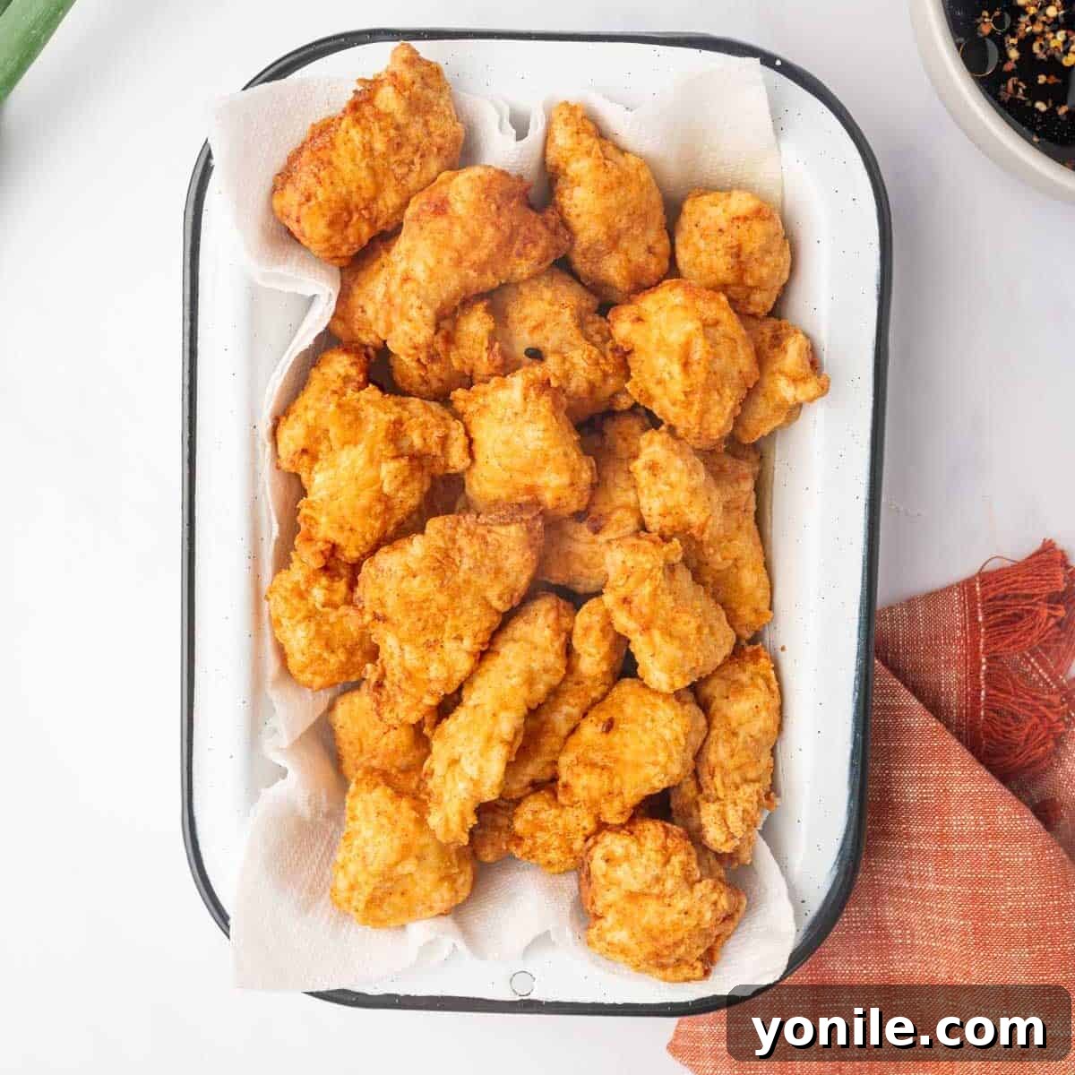 Fried chicken pieces drain on a paper towel on a tray.