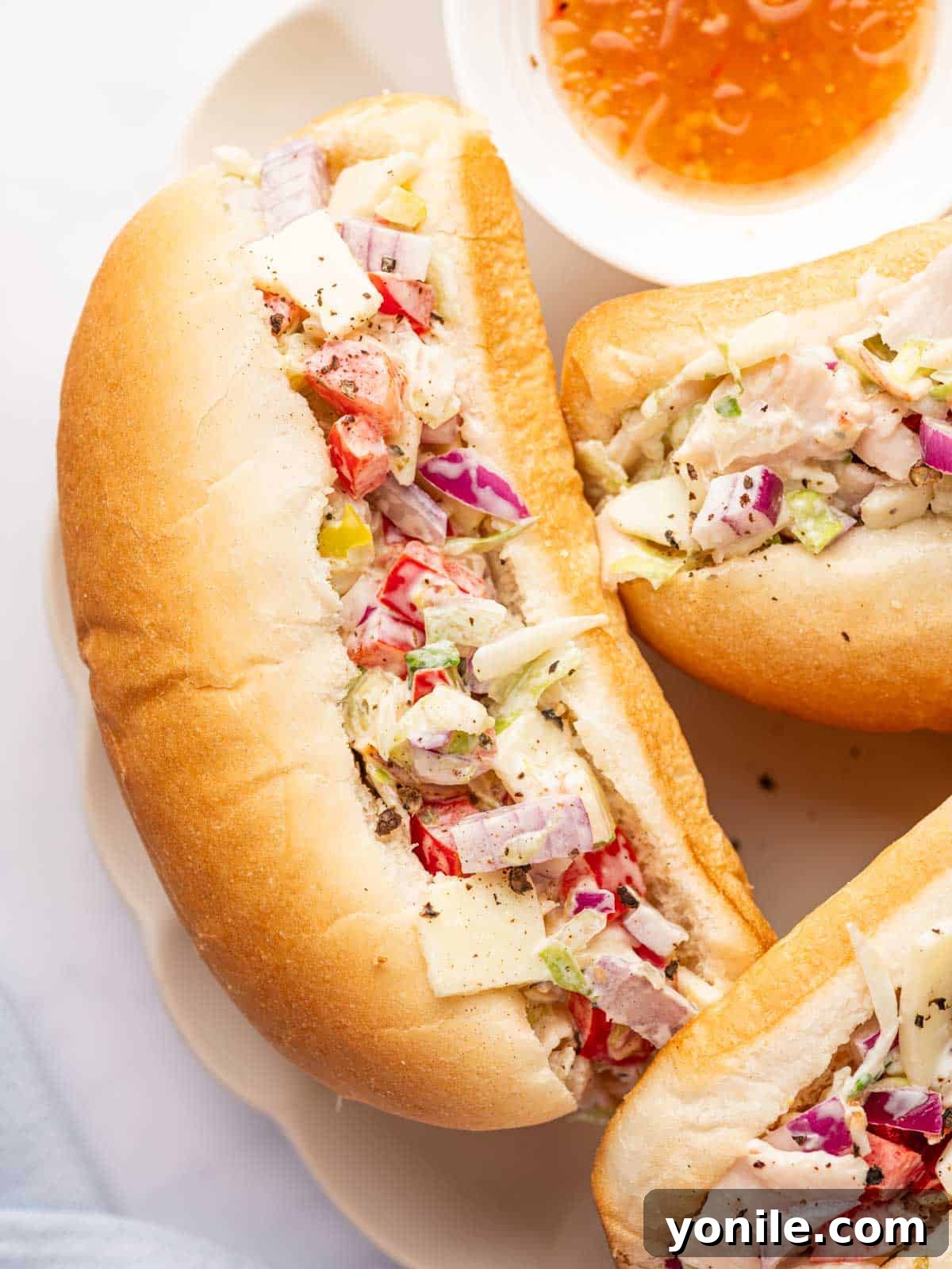 Zesty Chopped Italian Hero 9 A close-up view of three sub rolls filled with abundant chopped meats, cheese, and fresh veggies on a plate.