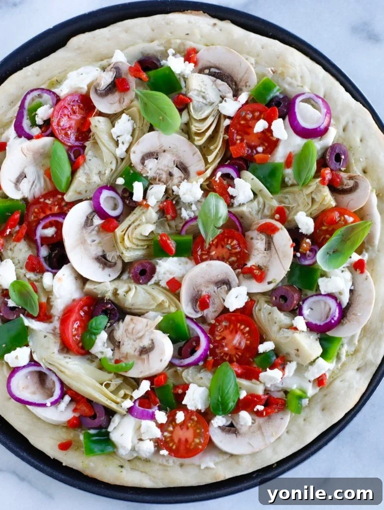 Top-down shot of Mediterranean Veggie Pizza, fully topped with vegetables and cheese, ready for final baking.