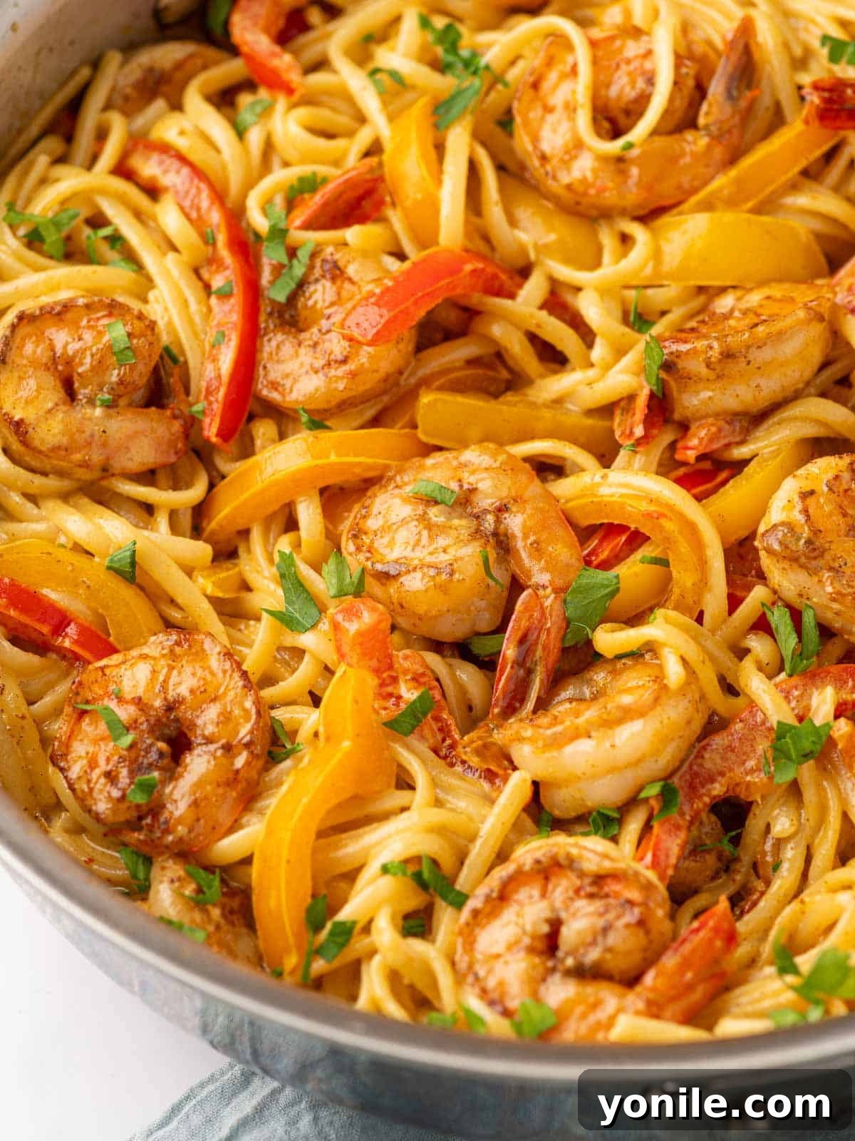 A tantalizing close-up shot of spicy shrimp, vibrant bell peppers, and creamy pasta, garnished with fresh parsley, highlighting the dish's rich textures and colors.