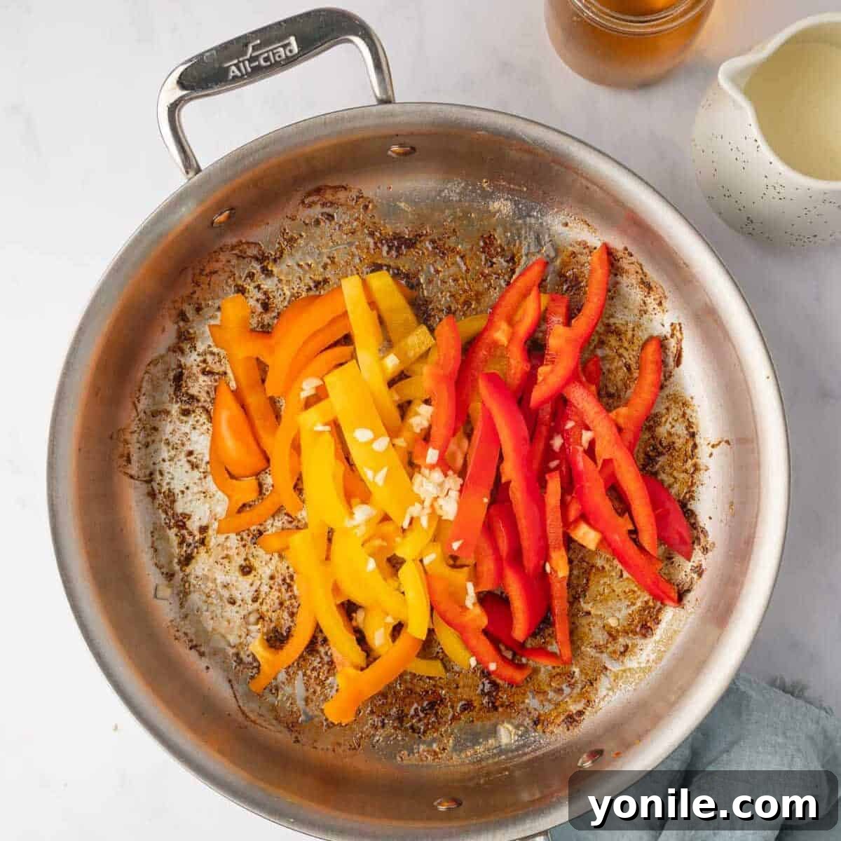 Colorful bell peppers are added to a hot skillet with melted butter and garlic, ready to be sautéed.